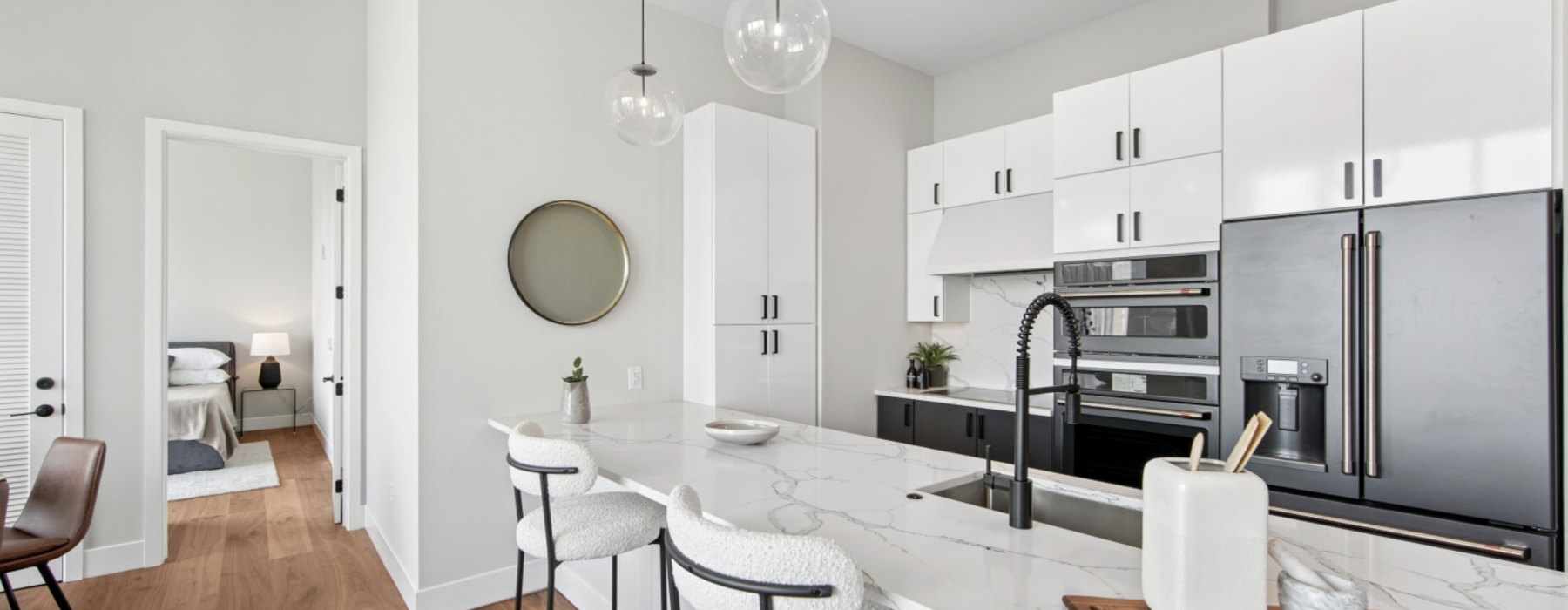 Modern kitchen with marble island, black appliances, and barstools. Bedroom in background.